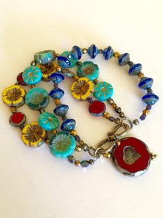 "Colorful bohemian style Czech glass multi strand flower bracelet with vintage bronze clasp and large Czech glass red heart bead charm. Bracelet is made of three separate but attached beaded strands of gorgeous Czech glass beads including: Sunflower yellow Picasso chunky pansy Cobalt blue Picasso UFO beads Turquoise/teal opaque gilded gold daisy coin beads Turquoise Hawaiian flower coral/teal/ turquoise beads Red Czech lentil beads Metallic bronze Czech fire polished faceted beads Gunmetal Czech Bohemian Jewelry With Heart Beads In Flower Shape, Bohemian Bracelets With Single Strand Round Beads, Bohemian Czech Glass Jewelry With Heart Beads, Bohemian Single Strand Bracelets With Round Beads, Bohemian Single Strand Beaded Bracelets As Gift, Bohemian Glass Jewelry With Heart Beads, Czech Beads Jewelry, Blue Picasso, Big Bracelets