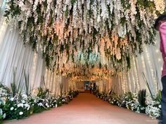 a man standing in front of a white flower covered tunnel with flowers hanging from it's ceiling