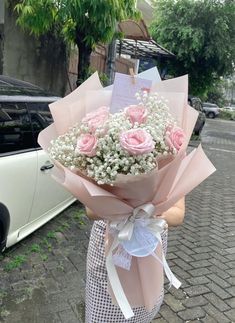 a bouquet of pink roses and baby's breath in front of a white car