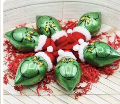 five green christmas ornaments with santa hats and grino's on them sitting in a pile of shredded red paper