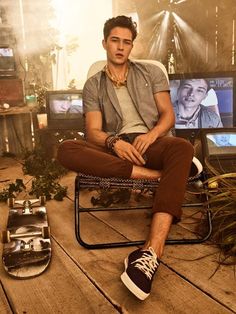 a man sitting in a chair next to a skateboard on the ground and two televisions behind him