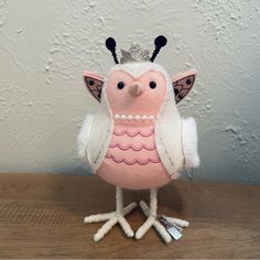 a pink and white owl with a crown on its head sitting on a wooden table