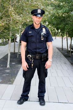 a police officer is standing on the sidewalk in front of some trees and bushes, smiling