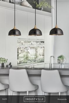 three lights hanging over a kitchen island with white chairs and bar stools in front of it