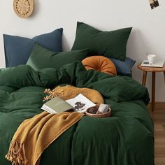 a bed with green sheets and pillows in a room next to a potted plant