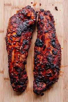 two pieces of meat sitting on top of a wooden cutting board next to each other