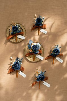 four small boutions with blue flowers on them sitting on a gold plate and brown table cloth