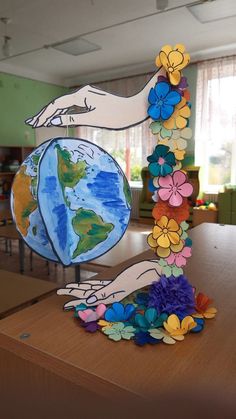 an art project made out of paper flowers and hands holding the world in each hand