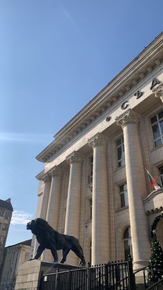 a statue of a lion in front of a large building with columns on the sides