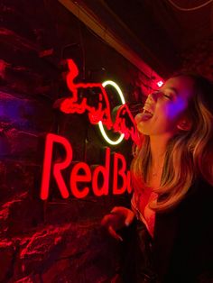 a woman standing in front of a red bull sign with neon lights on it's side