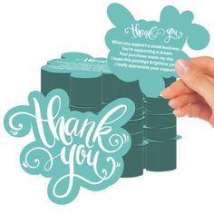 a hand holding up a thank card with the words thank you on it and some stacked stacks