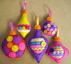 three colorful ornaments are hanging on a brown surface, one is decorated with buttons and the other has an ornament