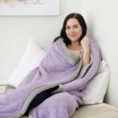 a woman sitting on a couch wrapped in a purple blanket and smiling at the camera