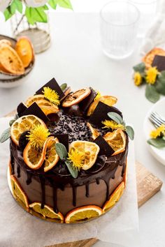 a chocolate cake with orange slices and flowers on top, sitting on a wooden cutting board