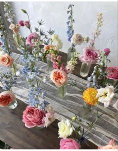 several vases filled with different colored flowers on a wooden table next to a mirror