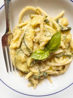 a white plate topped with pasta covered in sauce and spinach leaves next to a fork