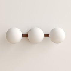 three white balls are hanging on the wall next to a wooden bar that is attached to it