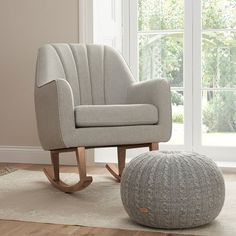 a rocking chair and footstool in front of a window with a white rug on the floor