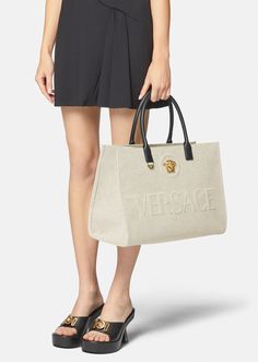 Crafted from canvas, this tote bag is adorned with a central La Medusa plaque and tonal debossed Versace logo lettering. The contrasting top handles are crafted from leather, and the spacious interior has two zipped pockets and a protector strap. Versace Tote Bag, Versace Bag, Versace Logo, Womens Designer Bags, Large Tote Bag, Leather Items, Large Tote, Canvas Tote Bag, Designer Bags