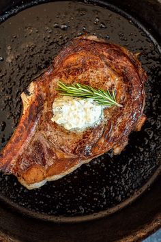 a piece of meat in a frying pan with butter and herbs on the side