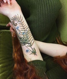 a woman's arm with a fern and blue flowers tattoo on her left forearm