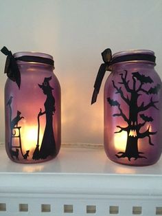 two mason jars decorated with halloween silhouettes and candles are sitting on a shelf next to each other