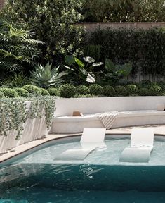 an outdoor pool with lounge chairs and greenery