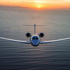 an airplane flying over the ocean at sunset