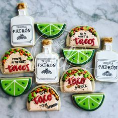 decorated cookies in the shape of liquor bottles and lime slices are arranged on a marble surface