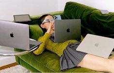 a woman laying on a green couch with two laptops in her lap and one is wearing sunglasses