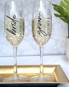 two champagne flutes sitting on top of a gold tray next to a potted plant