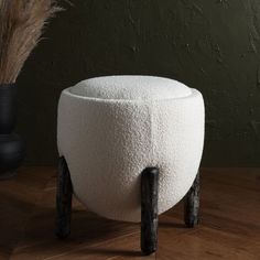 a white stool sitting on top of a wooden floor next to a vase with dry grass in it