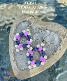 a pair of purple and white beaded earrings sitting on top of a heart shaped rock