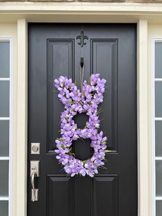 a purple wreath on the front door of a house that is decorated with lavender flowers