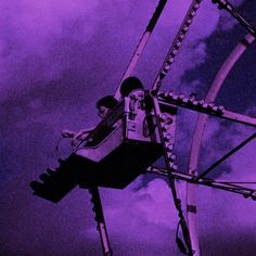 a man riding on top of a ferris wheel under a purple sky filled with clouds