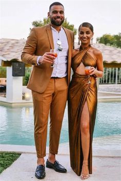 two people standing next to each other in front of a pool wearing brown outfits and holding drinks