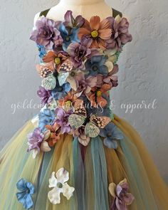 a dress made out of tulle with flowers and butterflies on the front, sitting on a mannequin