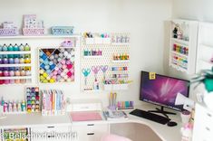 a desk with a computer and lots of crafting supplies on the shelves above it