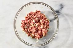 a glass bowl filled with ground meat on top of a marble countertop next to a wooden spoon