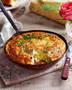 an omelet with cheese and herbs in a pan next to a knife on a cutting board