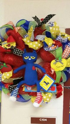 a red and green wreath with a blue cat on it's side, sitting in front of a door