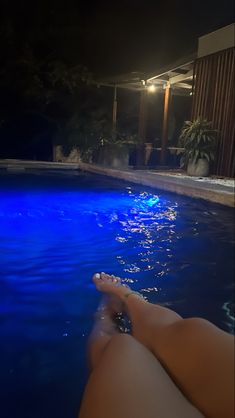 a person laying in the water near a swimming pool at night with their feet up