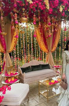 a woman standing in front of a couch under a flower covered canopy with flowers hanging from the ceiling