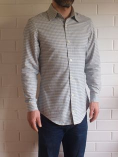 a man standing in front of a white brick wall wearing a blue and grey checkered shirt