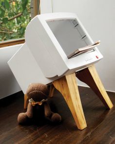 an old computer sitting on top of a wooden table next to a teddy bear in front of a window