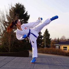 a woman in white and blue karate outfit doing a kick on the street with her leg up