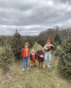 three children standing next to each other in a christmas tree farm