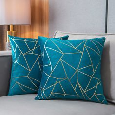 two blue pillows sitting on top of a gray couch next to a light brown lamp