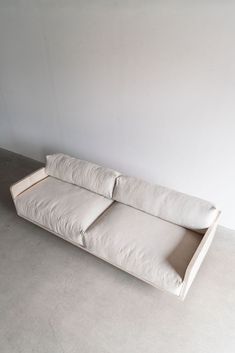 a white couch sitting on top of a cement floor next to a wall with no one in it