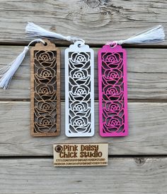 three bookmarks with pink, black and white designs hanging from tassels on wooden boards